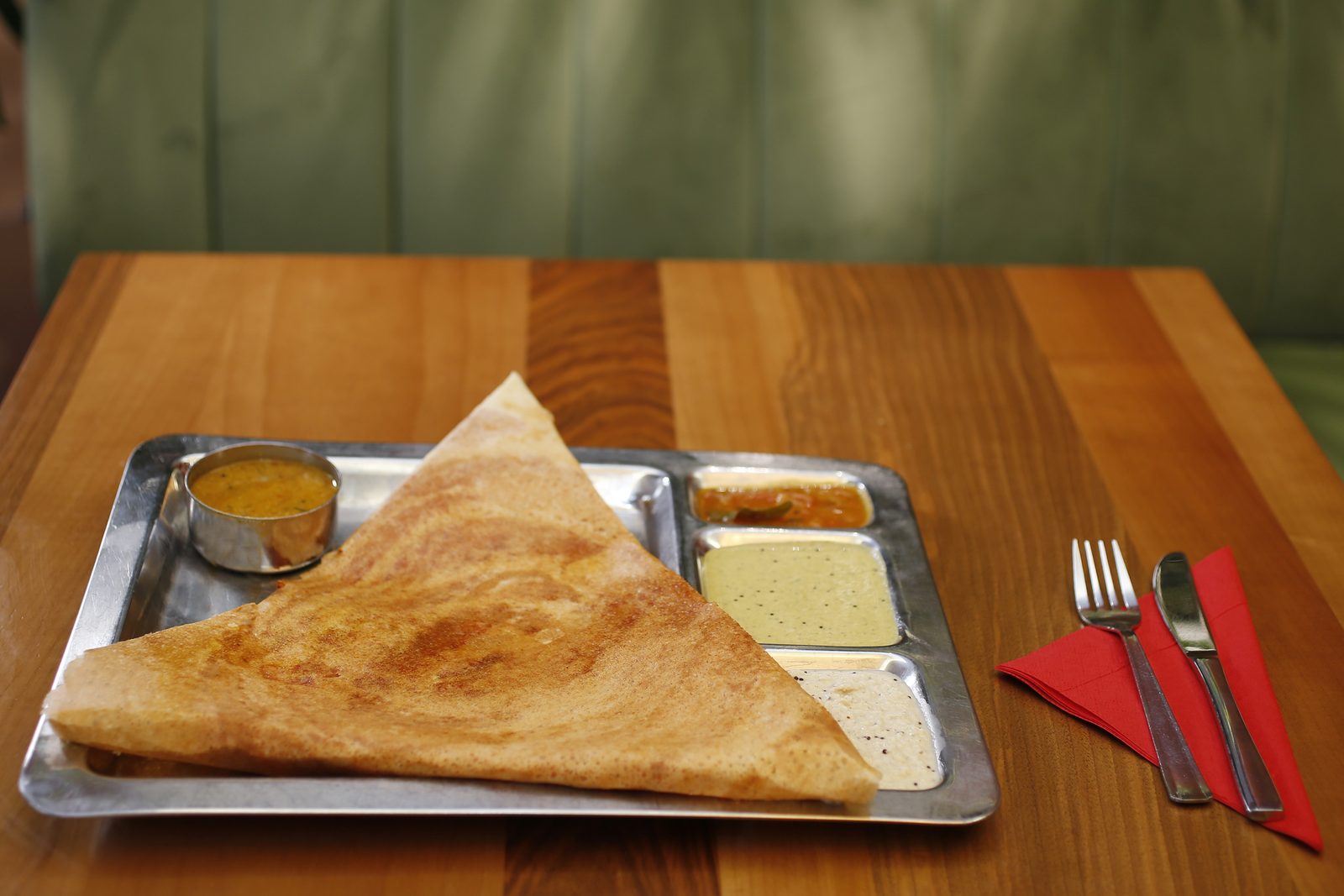 Dreieckig gefaltete Dosa auf einem Stahltablett mit Sambar und drei Chutneys.