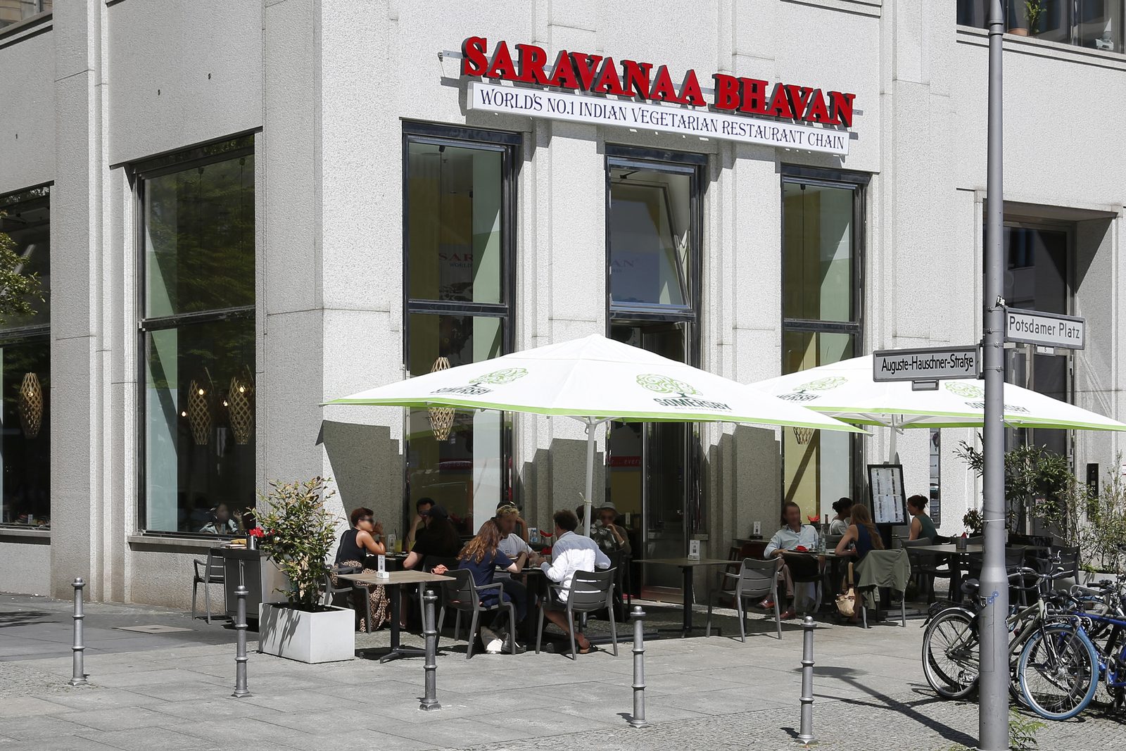 Corner building at Potsdamer Platz with the red Saravanaa Bhavan lettering, white parasols and guests on the terrace below.