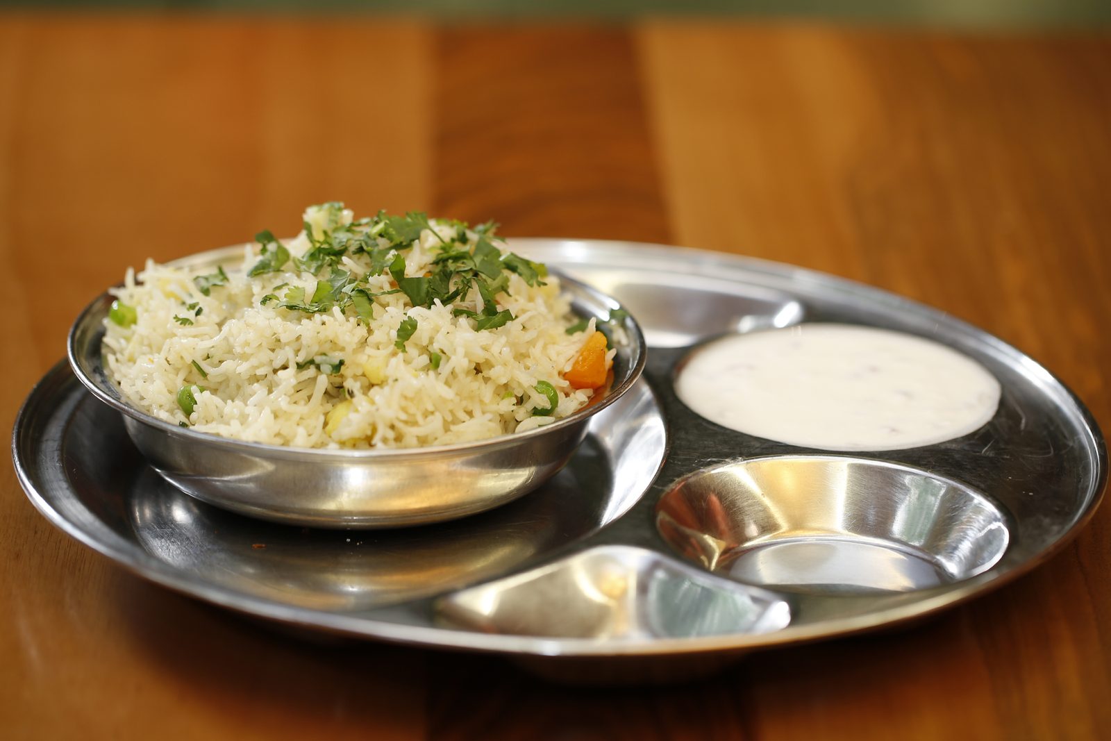 Thali mit Gemüsereis, Raitha und kleinen Schälchen.